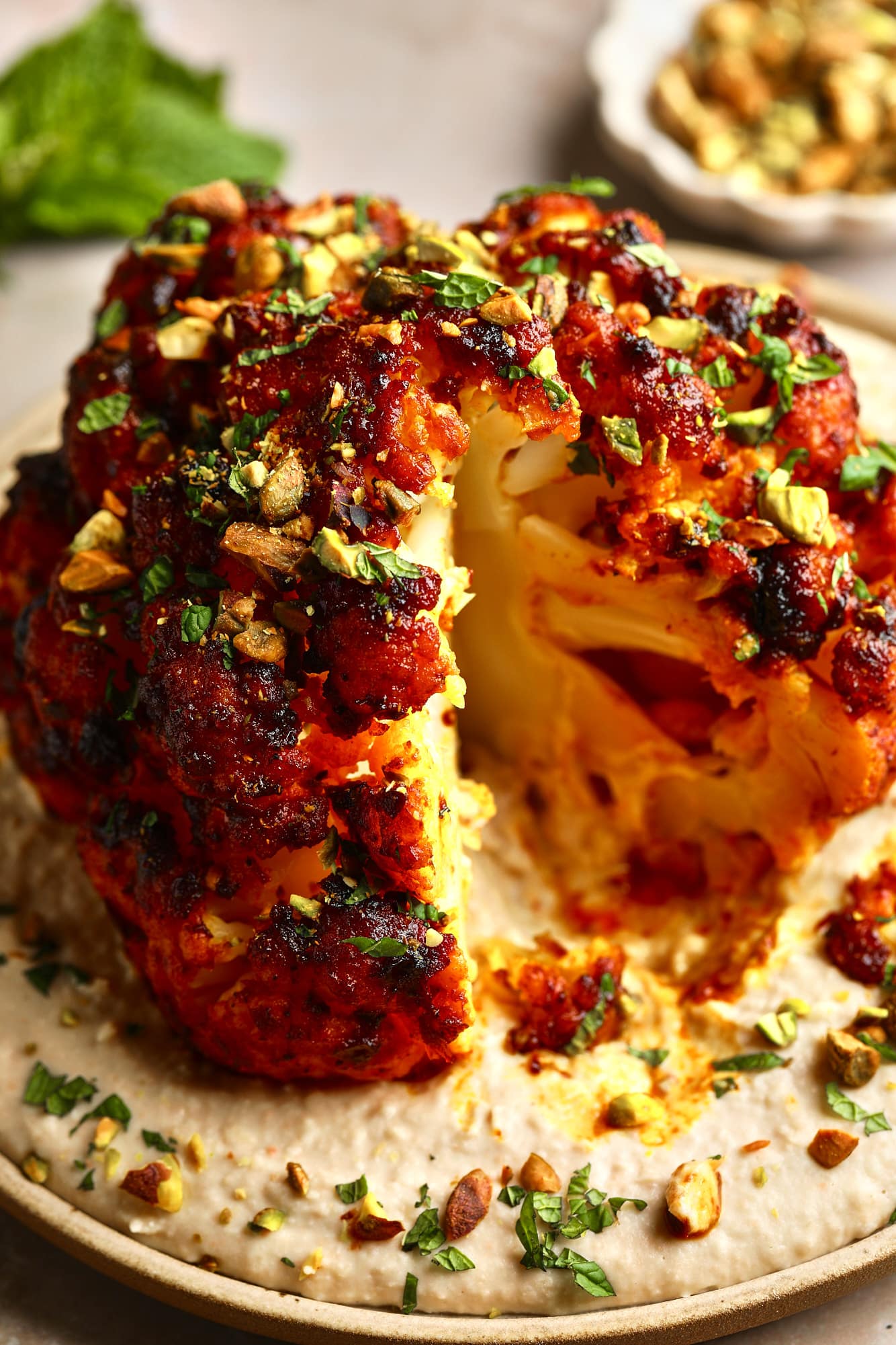 Near a sliced ​​sliced ​​roast cauliflower head on a white bean spread over a plate.